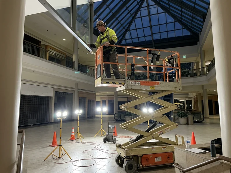 Glazier on a scissor lift inspecting mall atrium glazing after hours